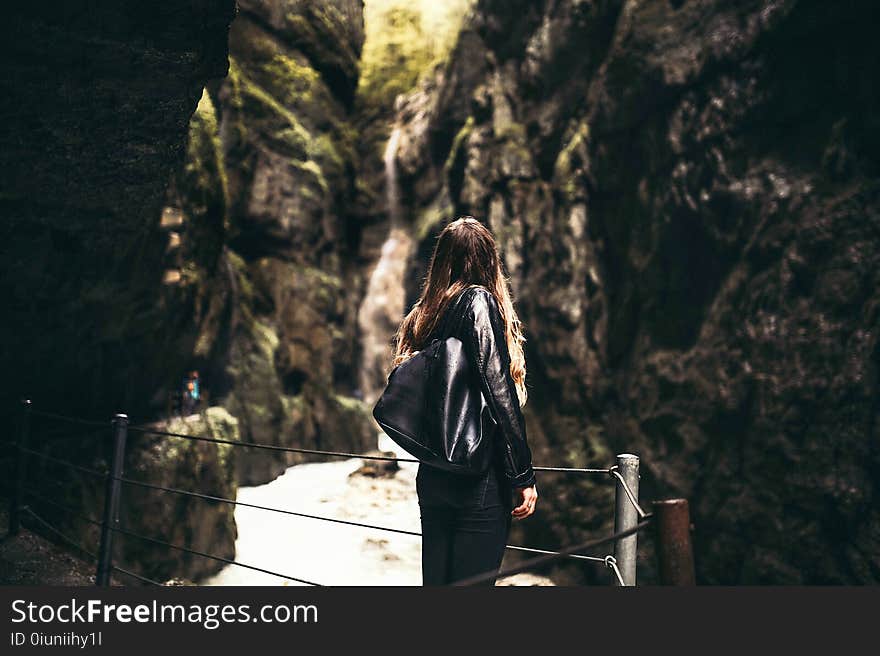 Woman in Black Leather Jacket Standing in Front of Gray Fence