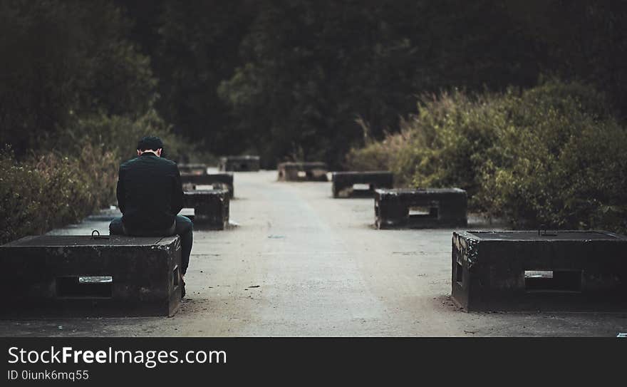 Man in Black Dress Shirt With Blue Denim Shirt Sitting on Black Concrete Bench Near Green Plants