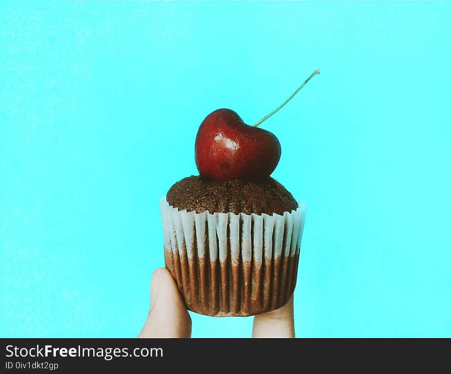 Person Holding Chocolate Cupcake With Cherry Topping