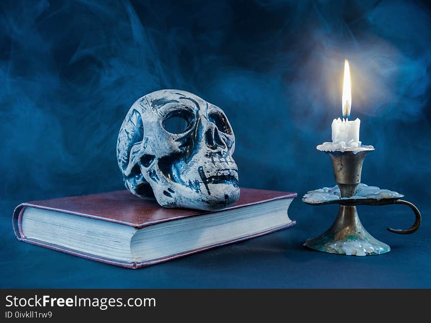 Gothic Skull On Old Book And Candle In Candlestick On Dark And Smoked Background