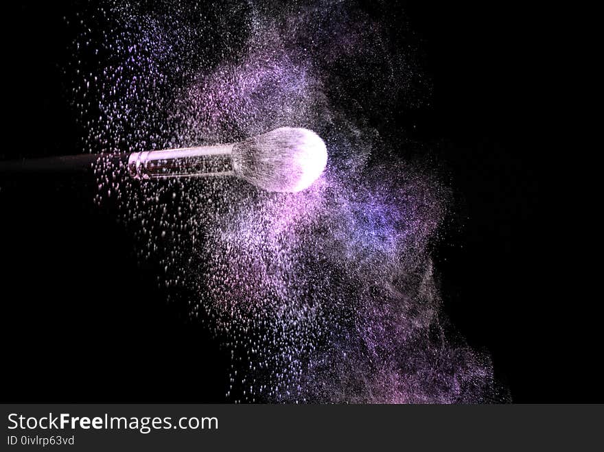 Make up brush and powder explosion dust in purple and pink color, selective focus, close up. Beauty and makeup concept image.