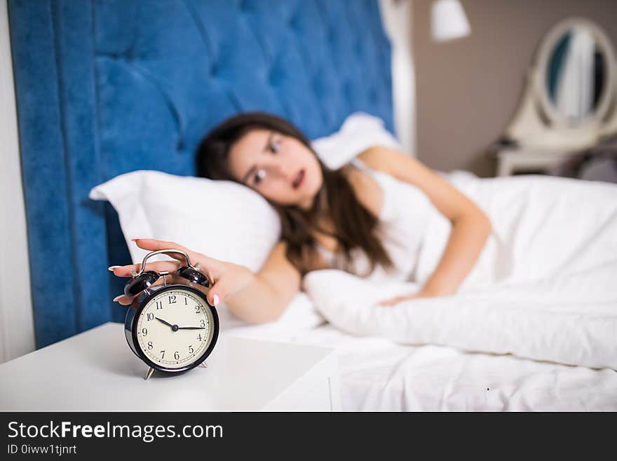 Sleepy young beauty woman stretching hand to ringing alarm to turn it off. Early wake up, not getting enough sleep, getting work c