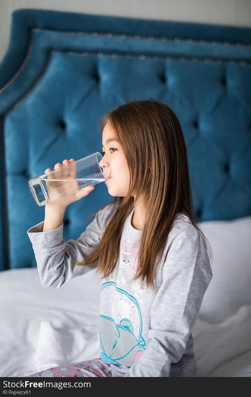 Beautiful Little Girl Drinking Water On White Bed At Home