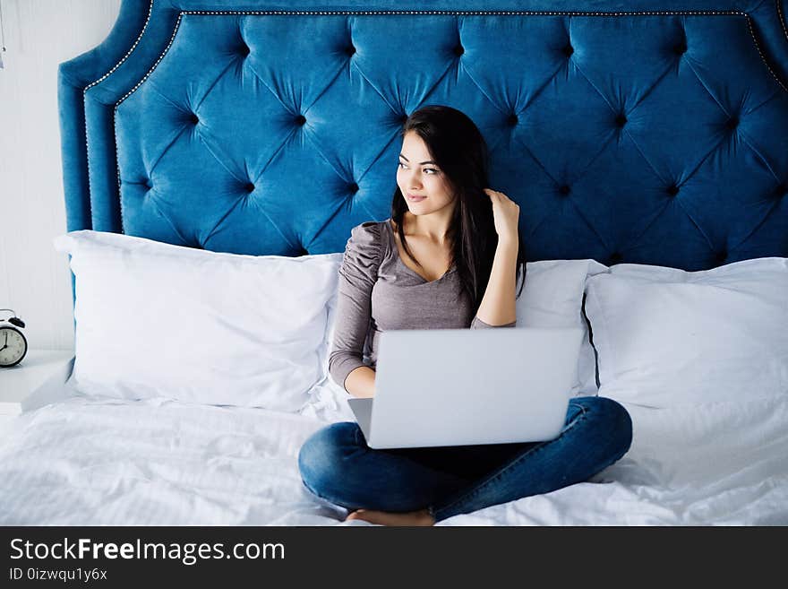 Portrait of beautiful happy young woman lying in bed and using laptop at home