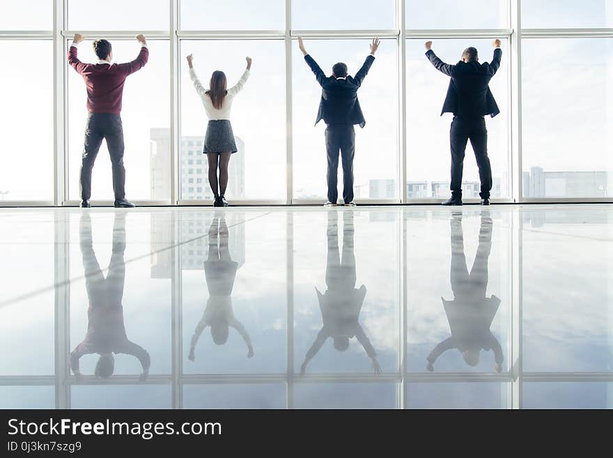 Successful group of business people in office in front of sunshine lit window with arms wide open celebrate victory. Welcoming new