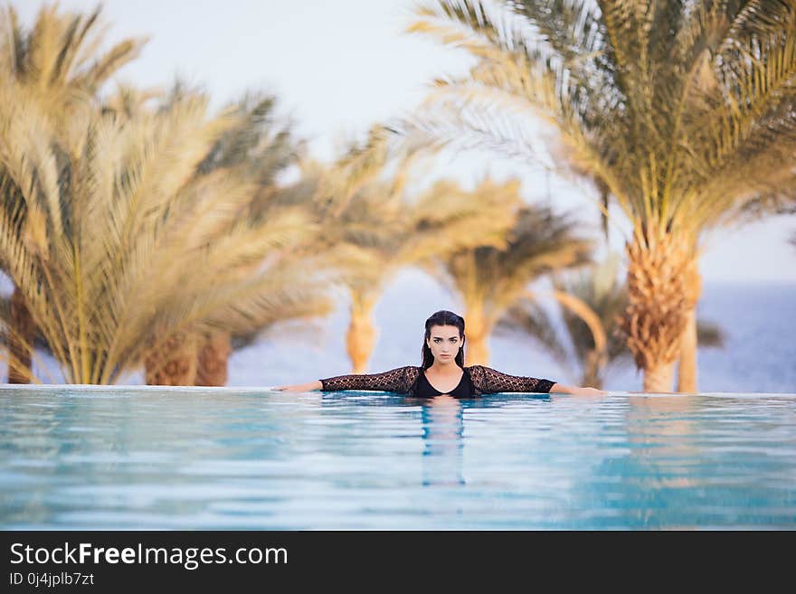 Portrait brunette woman relax in the water of infinity poolwith hands on edge luxury resort, infinity sea view