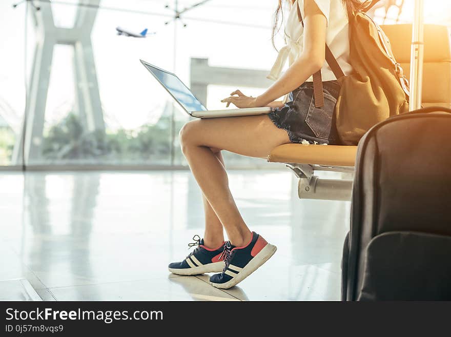 Asian teenage girl is using a laptop to check email or social network or internet at the international airport to travel on weekends.