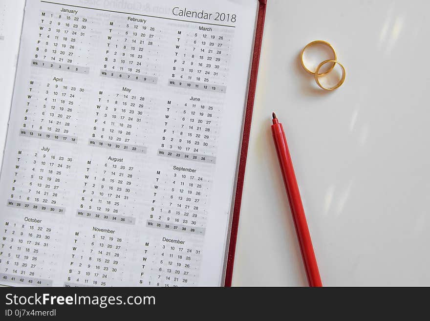 Planning a wedding in 2018. Calendar of 2018, two wedding rings and a pen on white background, space for text. Planning a wedding in 2018. Calendar of 2018, two wedding rings and a pen on white background, space for text