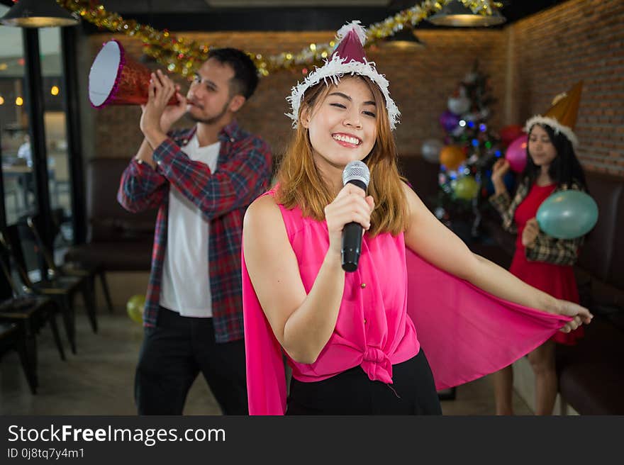 Asian women singer in santa claus hat with a microphone singing and dancing in Christmas party and friend in restaurant. concept of Xmas party, Christmas party and New year party celebration. Asian women singer in santa claus hat with a microphone singing and dancing in Christmas party and friend in restaurant. concept of Xmas party, Christmas party and New year party celebration.