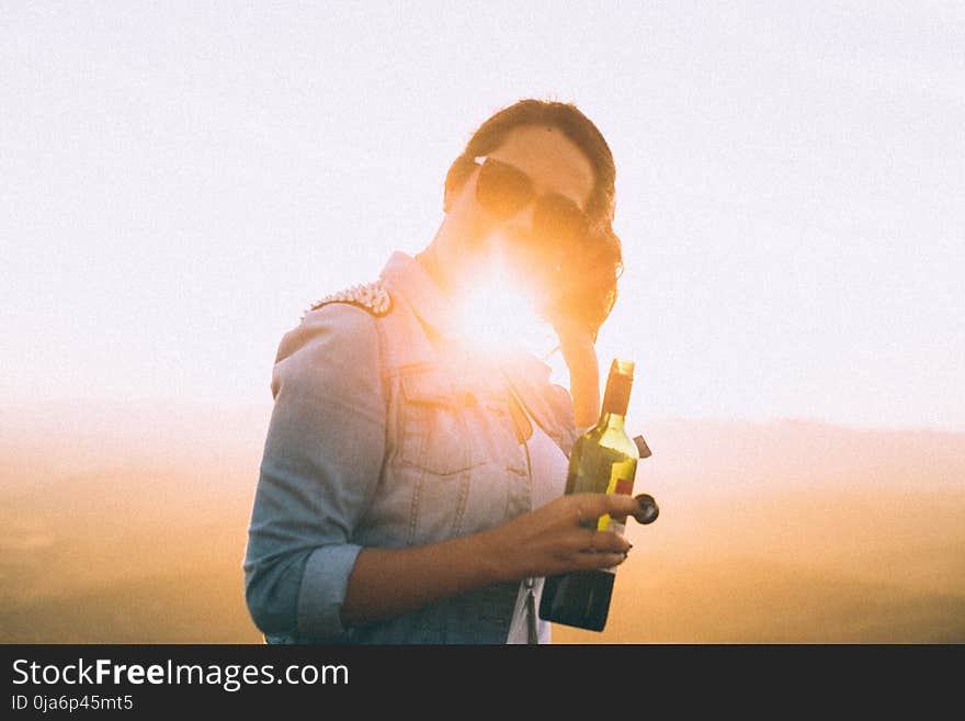 Woman Wearing Blue Denim Jacket Holding Wine Bottle in Golden Hour Photo