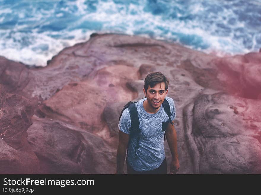 Photo Of Man Wearing Blue Shirt And Backpack Near Ocean