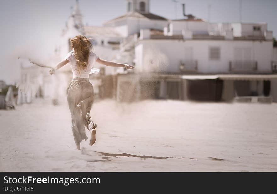 Woman Running on Sand Near White Concrete Building