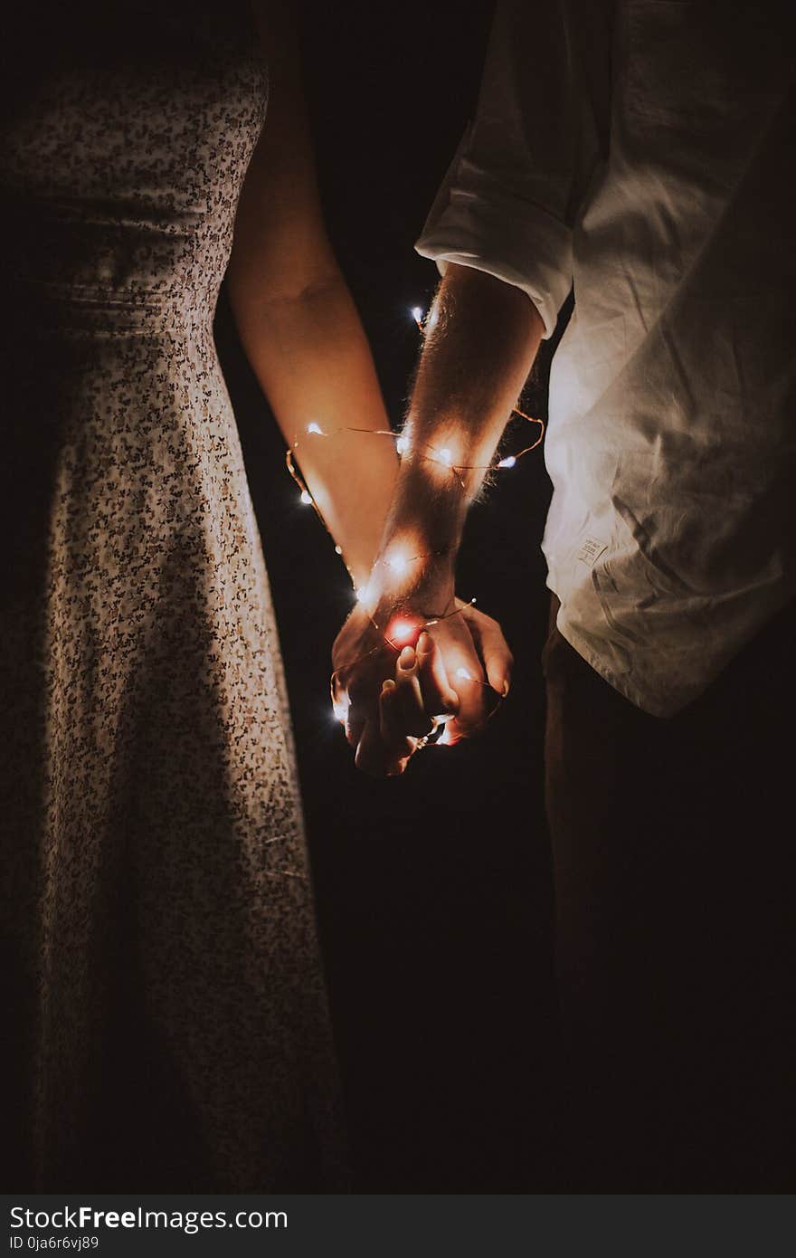 Man and Woman Holding Each Others Hand Wrapped With String Lights