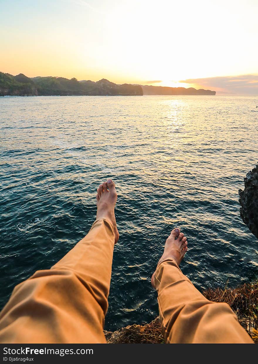 Person Wearing Yellow Pants Sitting on Rock Surrounded by Sea