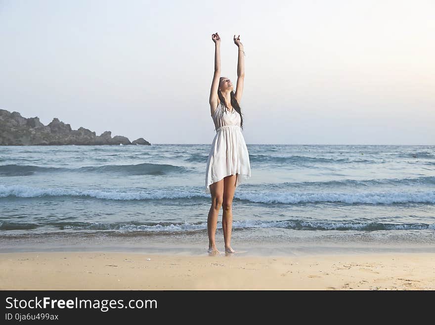 Photo of Woman in White Sleeveless Dress Raising Hands