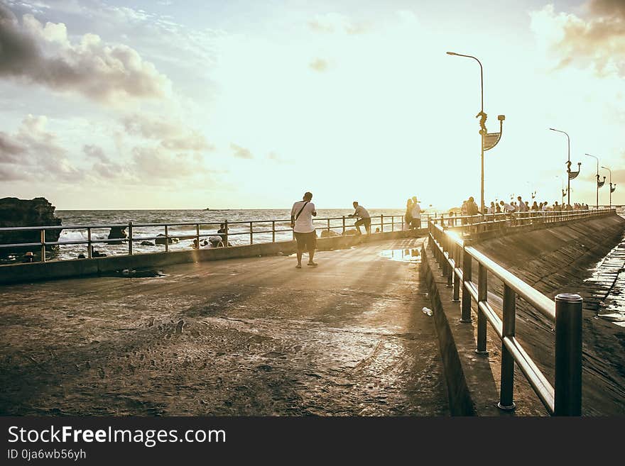 Man Wearing White Shirt Walking on Concrete Pavement Near Sea