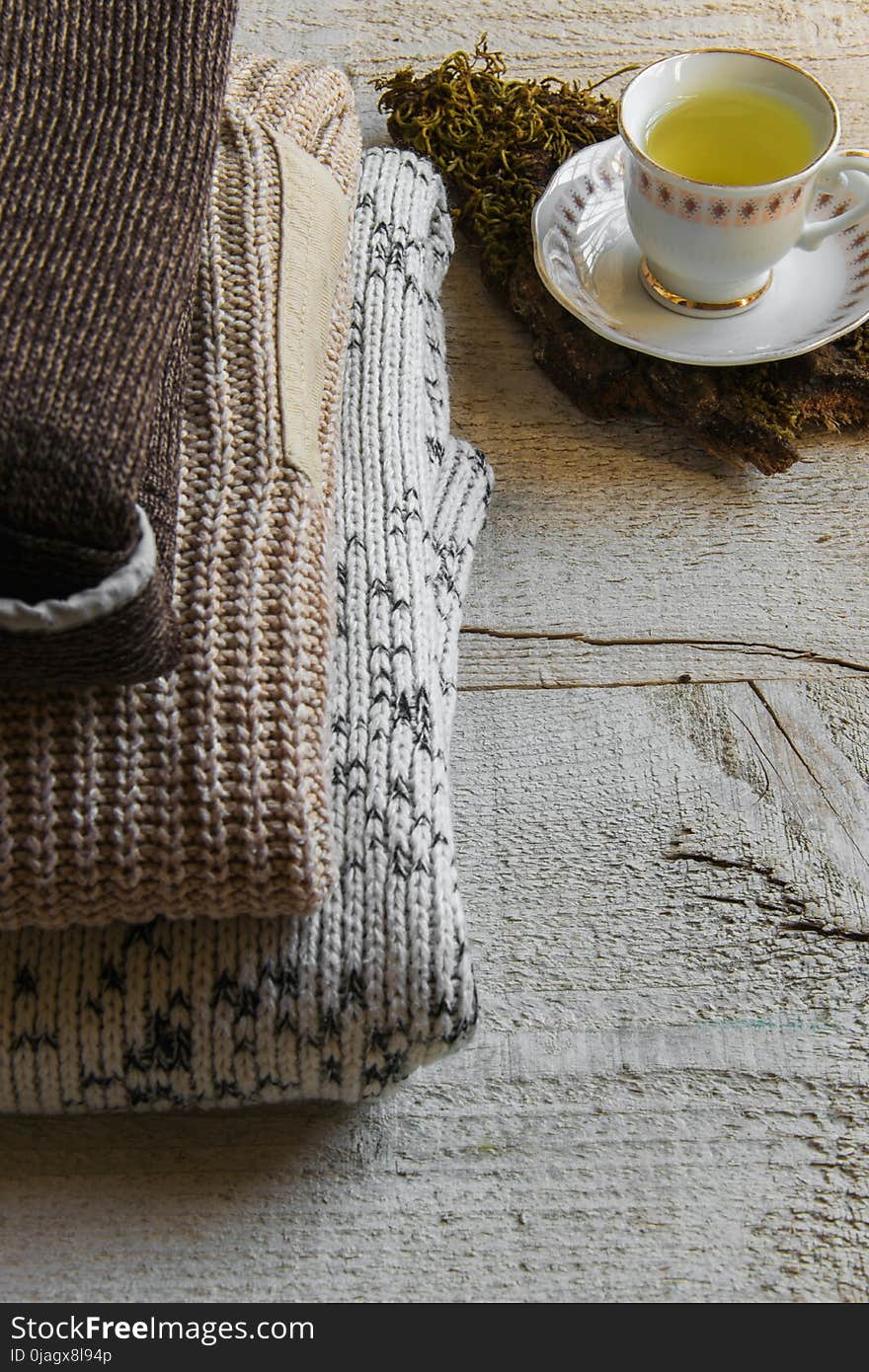 Cozy warm knitted maxi sweaters and cup of tea on wooden background with space for text. Concepts - fashion, comfortable time spent at home, rustic hygge life, relaxing