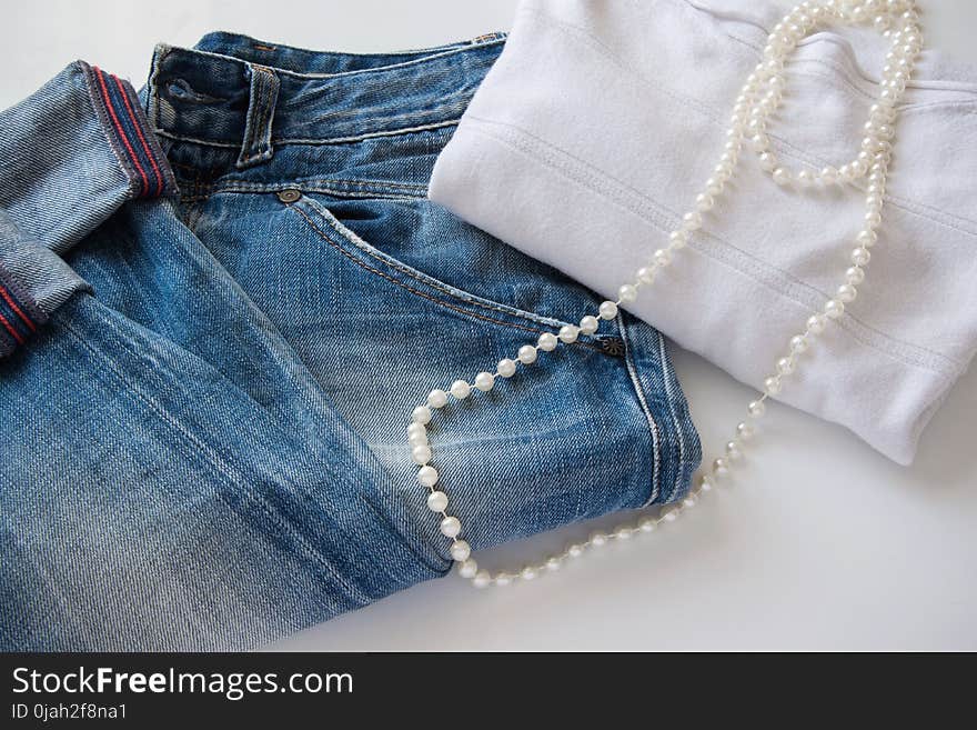 Women`s fashionable casual outfit - blue jeans, white sweater and white pearl necklace