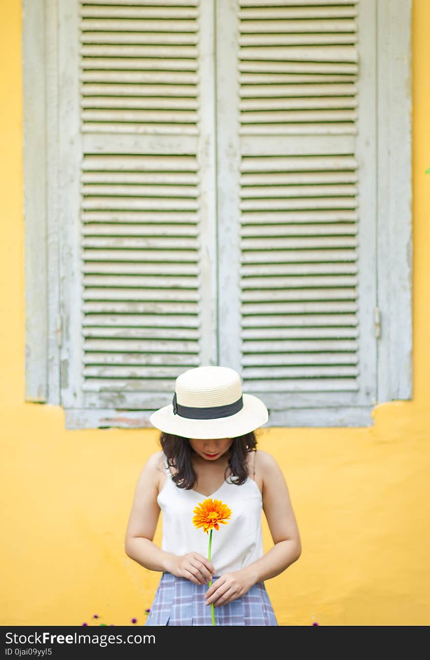 Woman in White Tank Top Holding Sunflower Near Window Outdoors