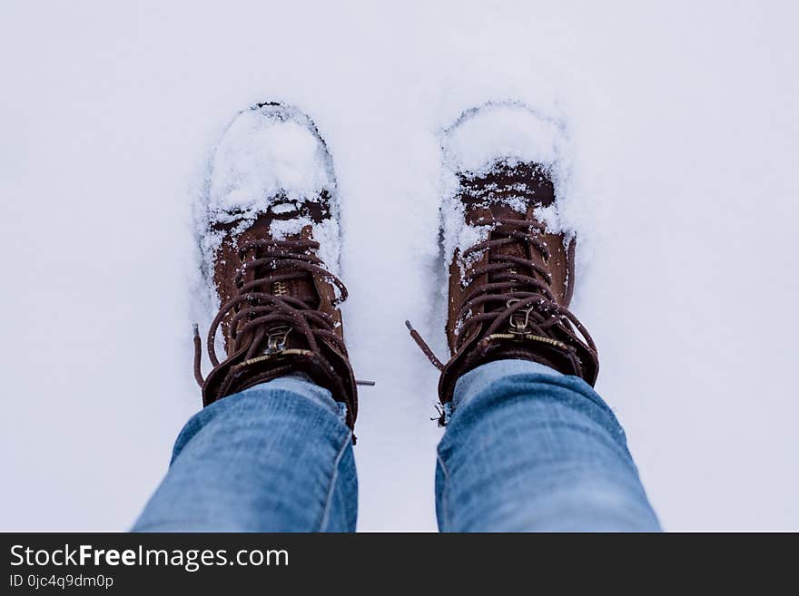 Person Wearing Brown Boots and Blue Denim Jeans Standing on Snow