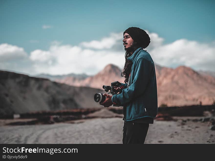 Man Wearing Jacket Holding Dslr Camera on Desert