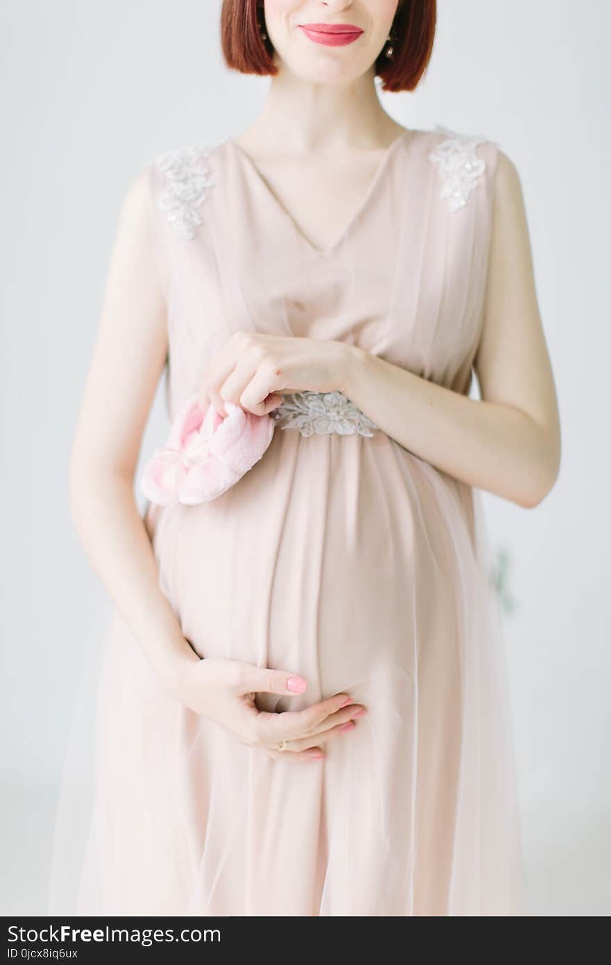 Pregnant girl is standing with pink shoes of baby on white background
