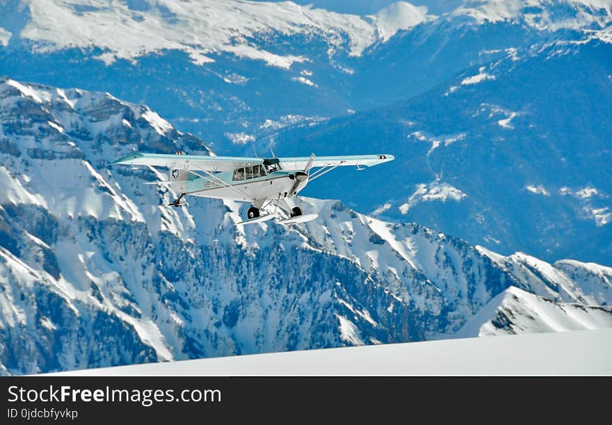 White and Green Monoplane Flying Above Mountains