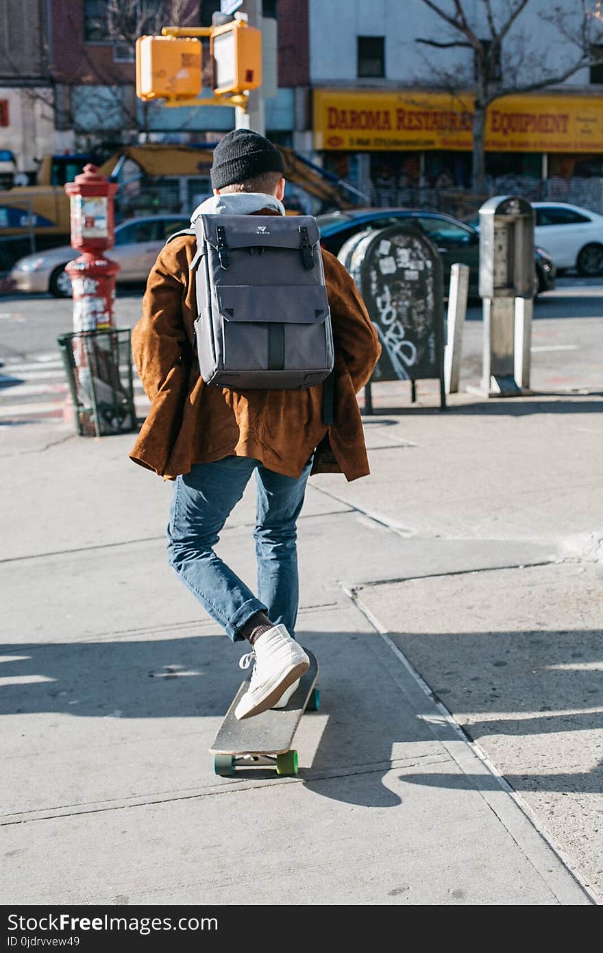 Man Wearing Brown Jacket, Blue Denim Jeans, and White Shoes Riding Skateboard on Sideway