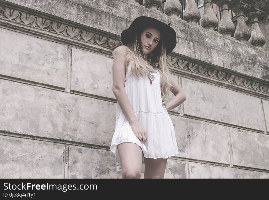 Woman in White Sleeveless Dress and Hat Near Wall