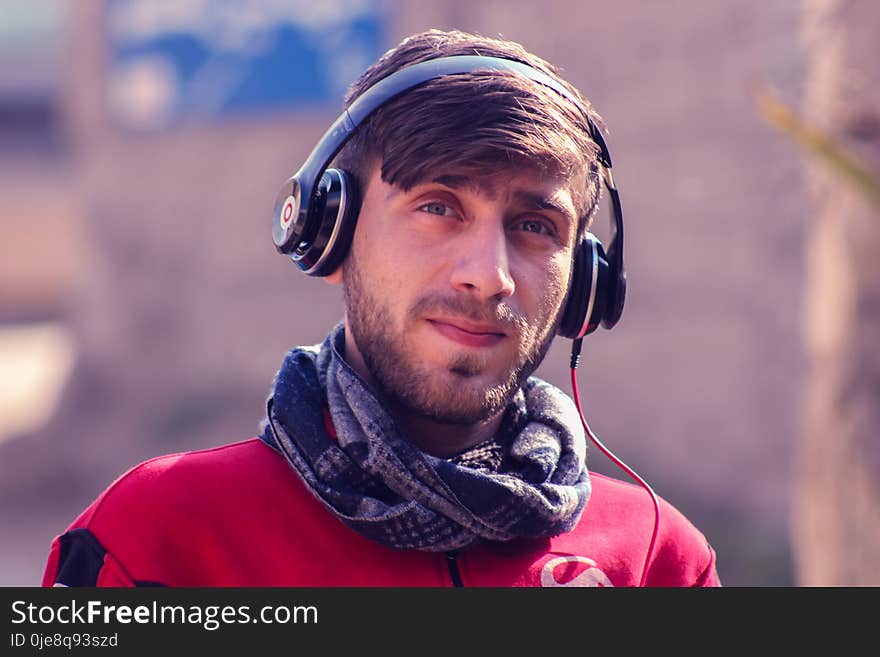 Closeup Photo of a Man Wearing Red Top, Gray Scarf, and Black Beats by Dr. Dre Headphones