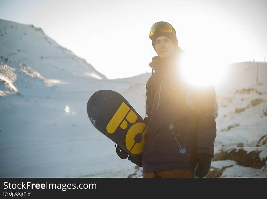 Man in Blue Pullover Hoodie Holding Blue and Yellow Snowboard