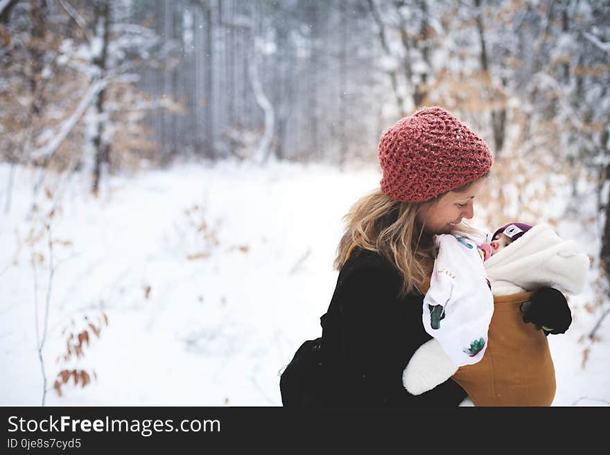 Woman in Red Knitted Cap and Black Top Holding Baby With Brown Carrier