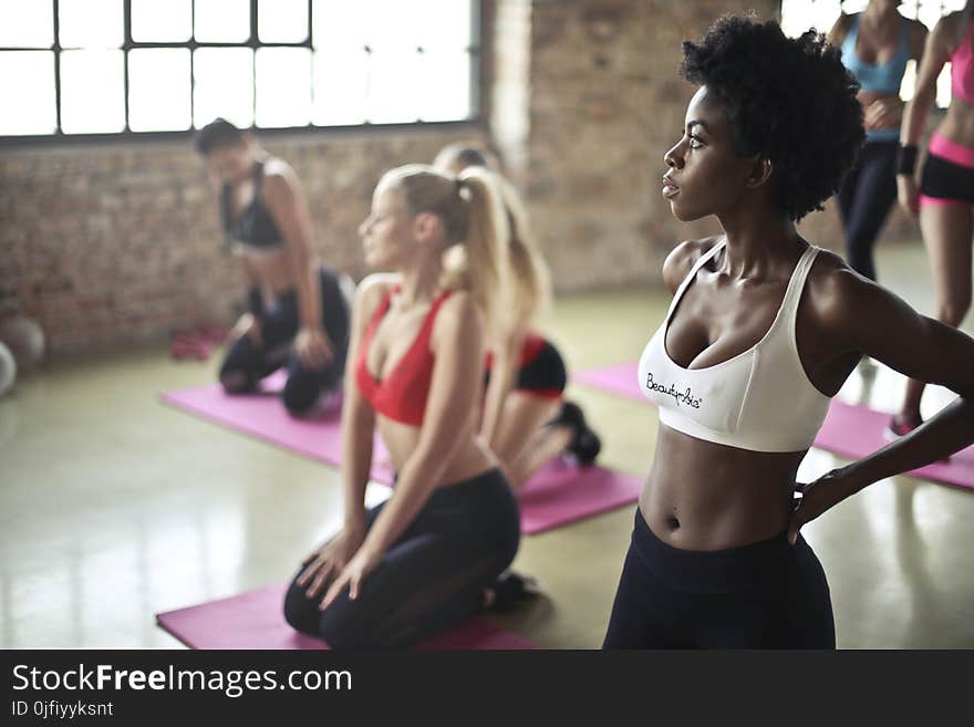 Selective Focus Photography of Woman in White Sports Brassiere Standing Near Woman Sitting on Pink Yoga Mat