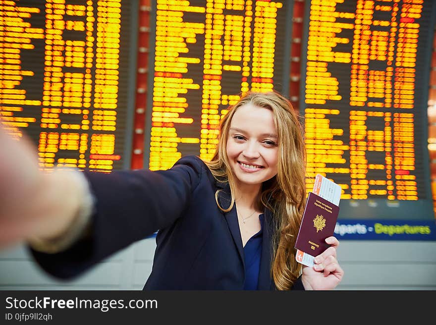 Young woman in international airport near large information display taking selfie