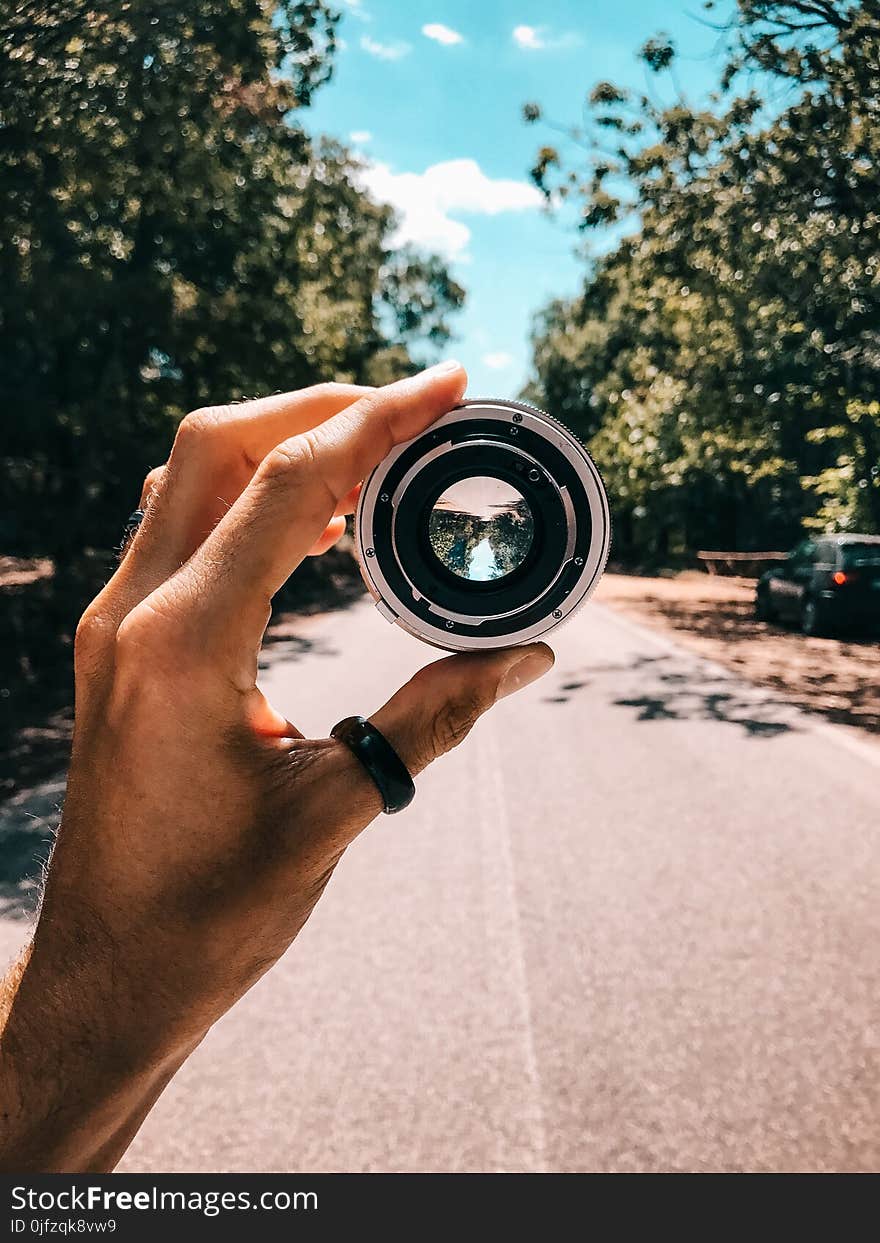 Person Holding Camera Lens in the Middle of Street Under Blue Sky