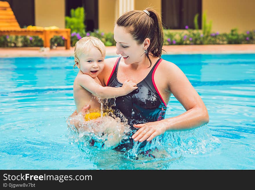 Young mother teach her little son, how to swim in a swimming pool.