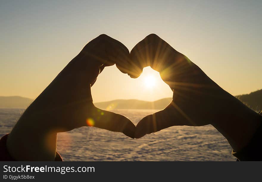 Young man and woman making a heart shape with her fingers. silhouette of hands. against the sunset