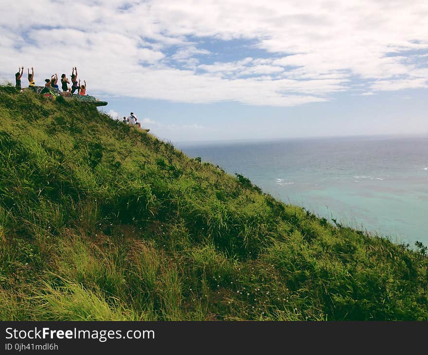 People Standing on a Green Mountain Peak Watching the Clear Blue Body of Water