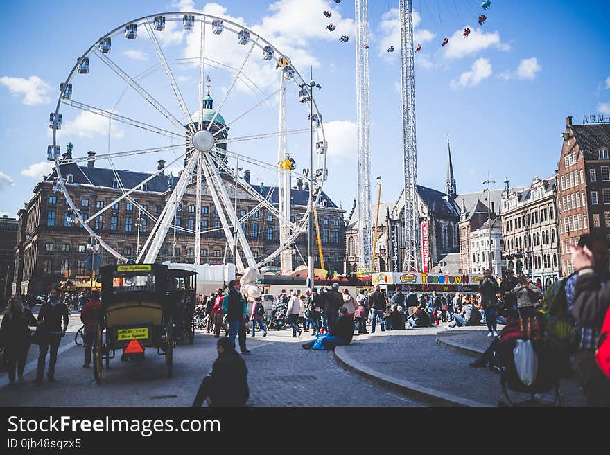 Ferris Wheel Beside Brown Buildings and People Under Blue Cloudy Sky at Daytime