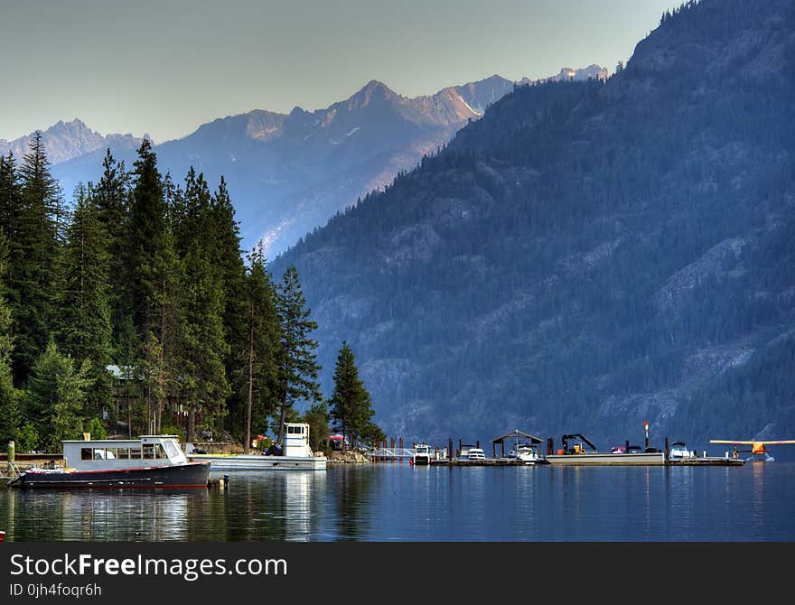 Body of Water Near Mountain Covered by Trees With Grey Clouds Above during Daytime