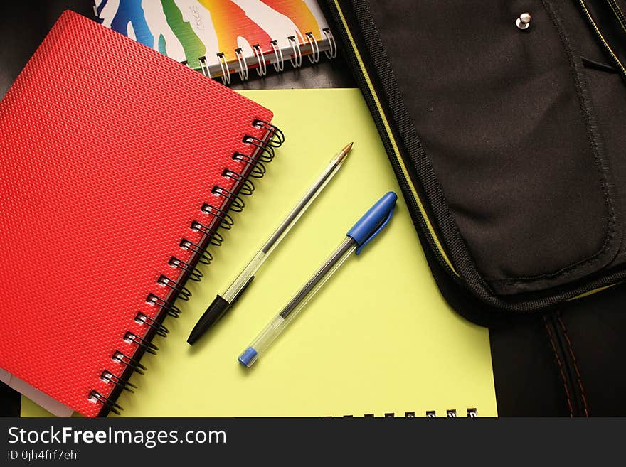 Black and Blue Pens Beside Red Covered Notebook