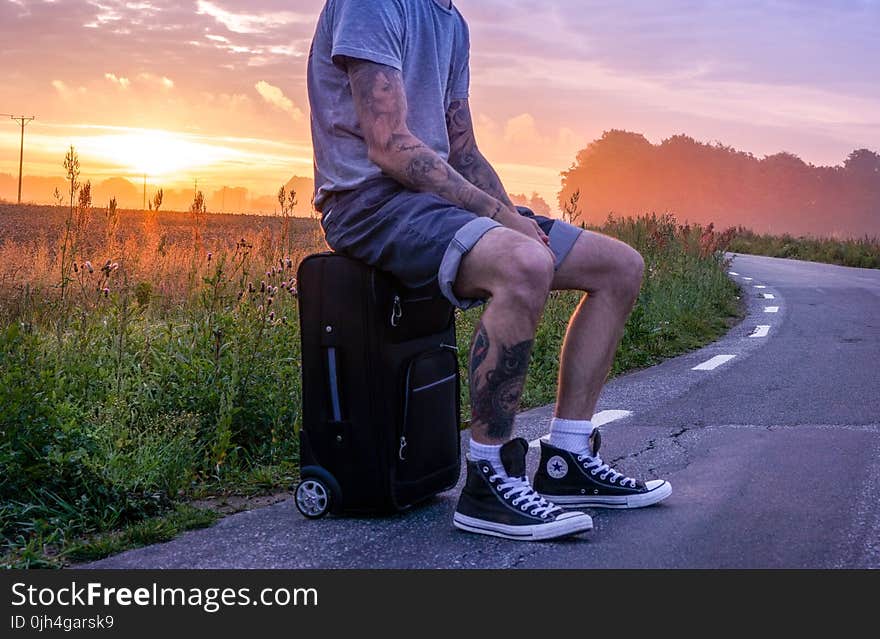 Man Sitting on Luggage on Road Side during Sunset