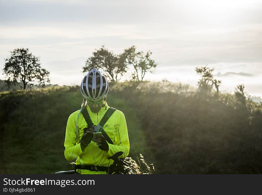 Man in Green Bicycle Suit Standing While Using His Smartphone