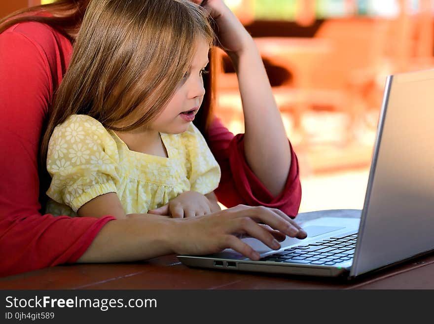 Brunette Woman in Red With Girl in Yellow on Lap Before Laptop