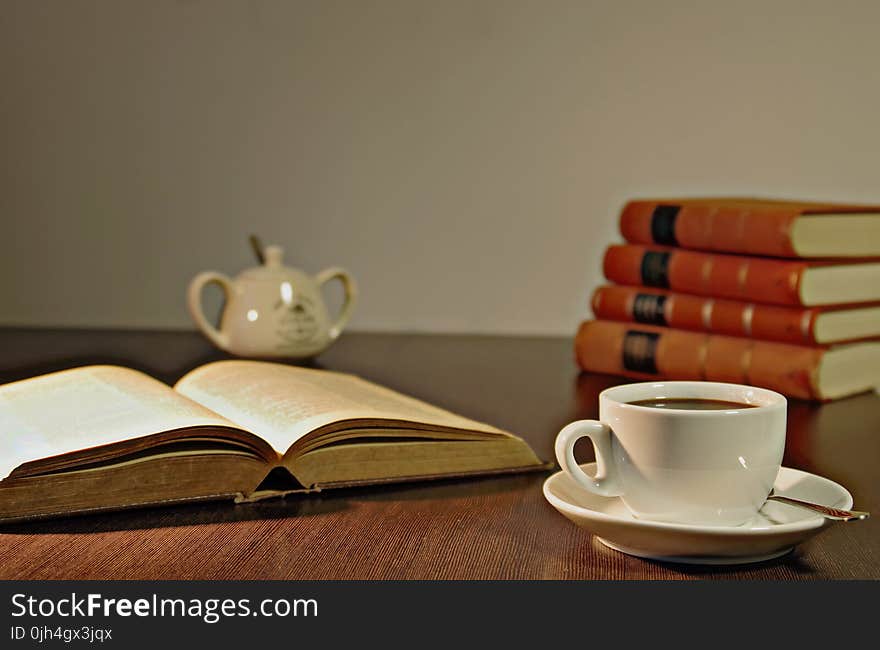 White Ceramic Teacup on Brown Wooden Table Beside Book