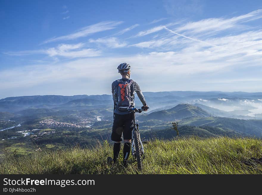 Biker Holding Mountain Bike on Top of Mountain With Green Grass