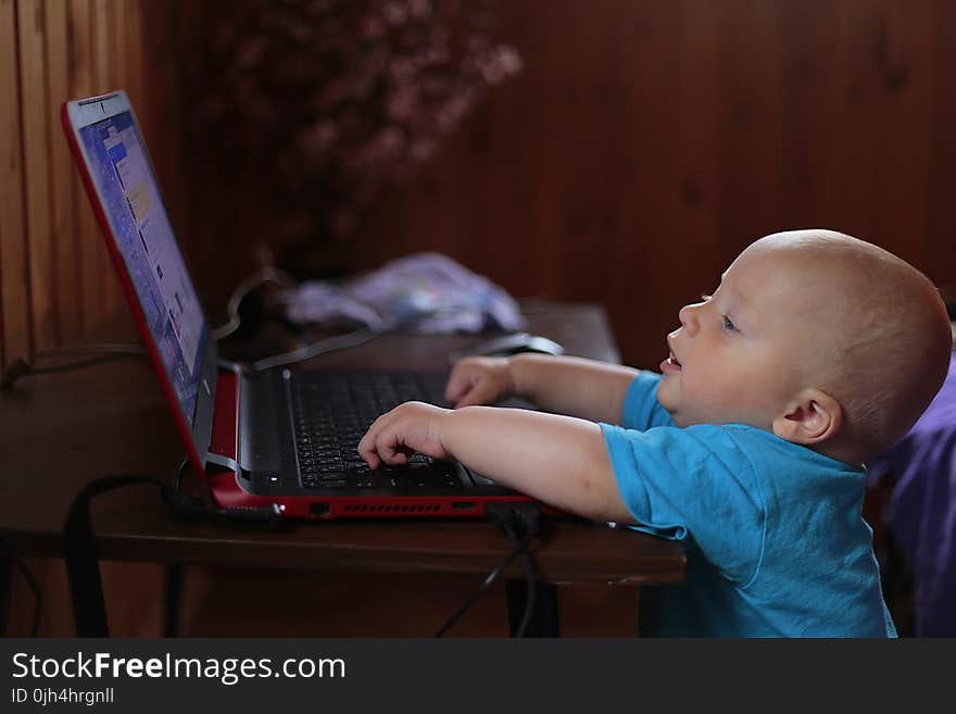 Boy Wearing Blue T Shirt Using Black Laptop Computer in a Dim Lighted Scenario