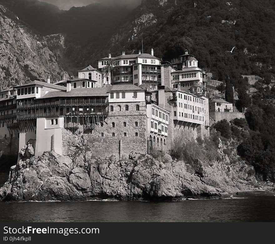 Landscape Photography of Gray and White House Near Mountain Cliffs Above Body of Water