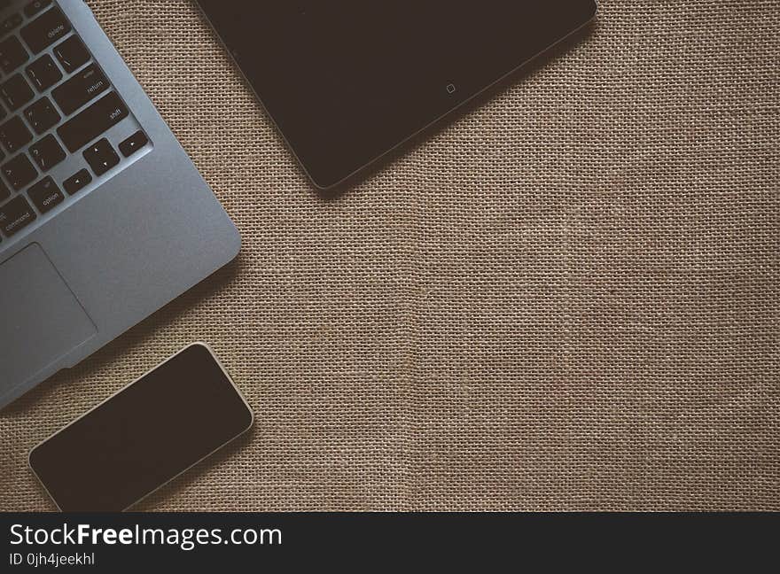 Black Ipad Near Macbook on Brown Textile