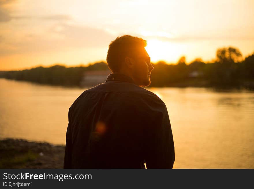 Man Sitting Near Large Body of Water Under Clear Sky during Sunset